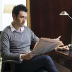 Young businessman reading newspaper in study